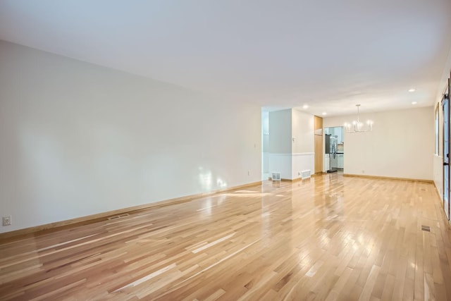 unfurnished room with a chandelier and light wood-type flooring