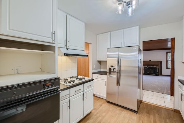 kitchen featuring white gas stovetop, black oven, stainless steel fridge with ice dispenser, white cabinets, and light hardwood / wood-style flooring