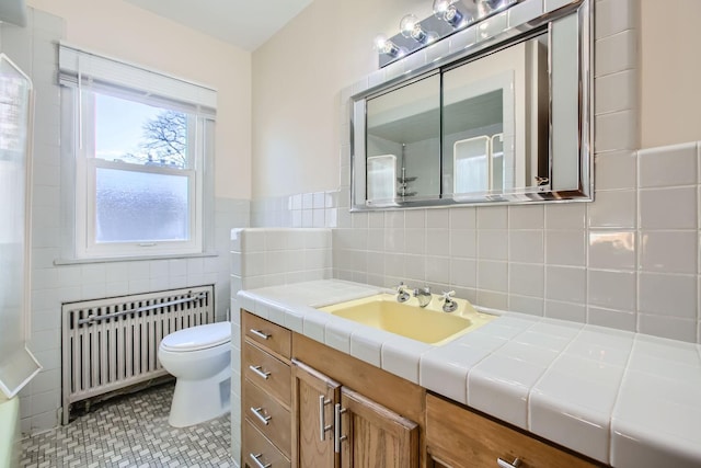 bathroom with tile walls, vanity, toilet, and radiator