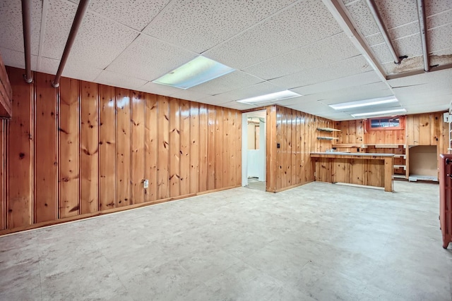 basement with a drop ceiling and wooden walls