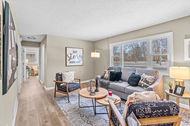 living room with a textured ceiling, light wood finished floors, and baseboards