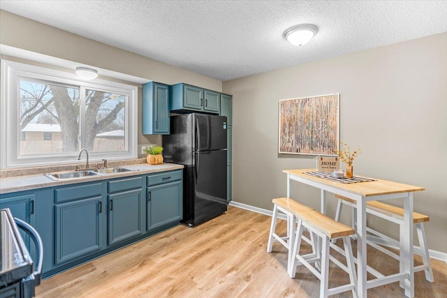 kitchen featuring light wood-style flooring, a sink, baseboards, light countertops, and freestanding refrigerator