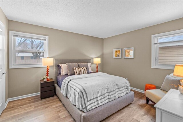 bedroom with light wood-style floors, baseboards, and a textured ceiling