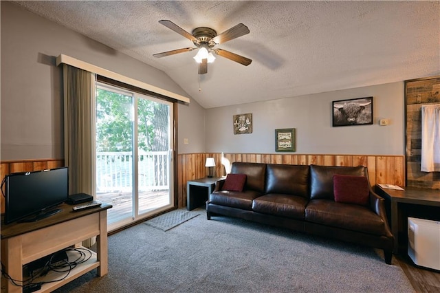 carpeted living room featuring a textured ceiling, wooden walls, vaulted ceiling, and ceiling fan