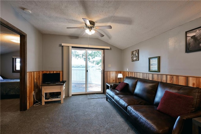 carpeted living room with wooden walls, vaulted ceiling, ceiling fan, and a textured ceiling