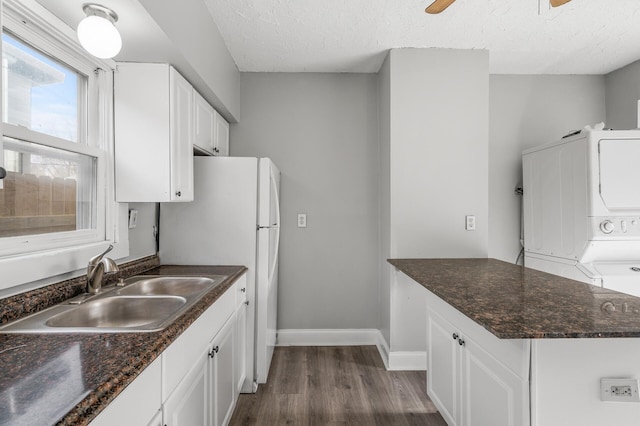 kitchen with sink, a textured ceiling, stacked washer and clothes dryer, and white cabinets