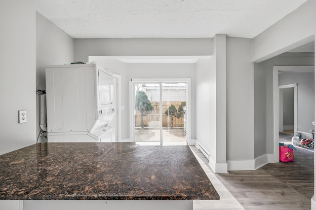 foyer featuring baseboard heating, stacked washer and dryer, a textured ceiling, and light wood-type flooring