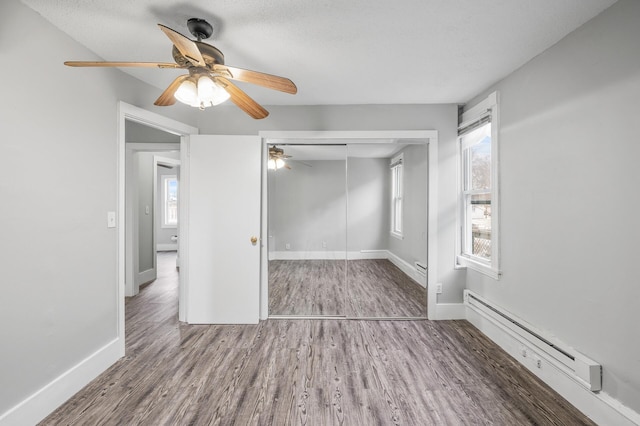 unfurnished bedroom featuring multiple windows, a baseboard radiator, a closet, and ceiling fan