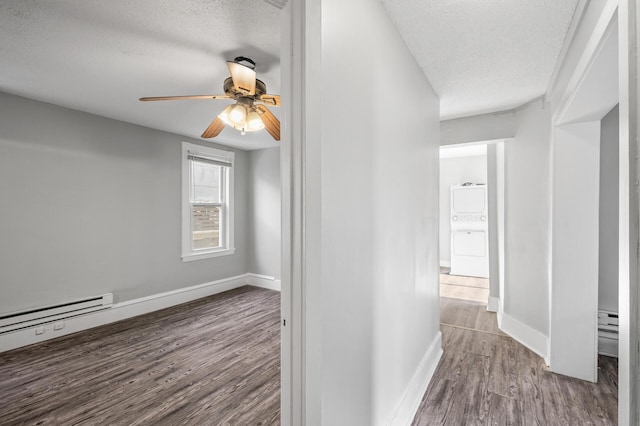 hall with baseboard heating, wood-type flooring, stacked washing maching and dryer, and a textured ceiling