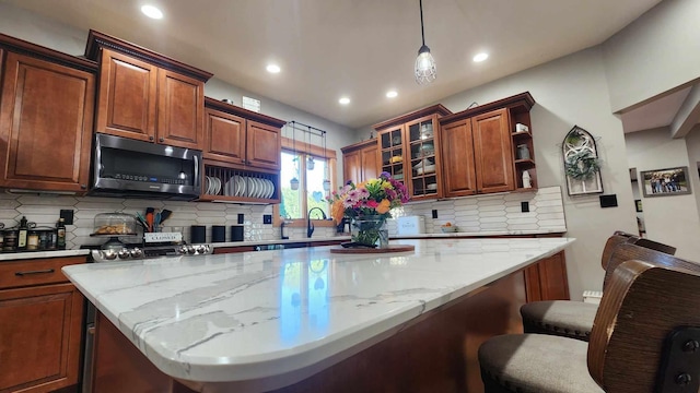 kitchen with a breakfast bar, backsplash, pendant lighting, and light stone counters