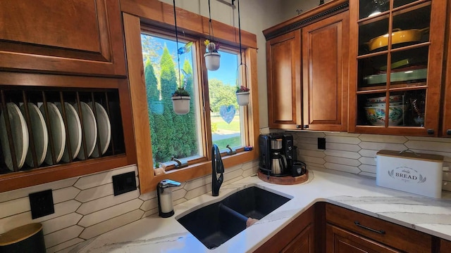 kitchen featuring hanging light fixtures, backsplash, sink, and light stone counters