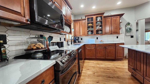 kitchen featuring appliances with stainless steel finishes, light hardwood / wood-style floors, light stone counters, backsplash, and sink