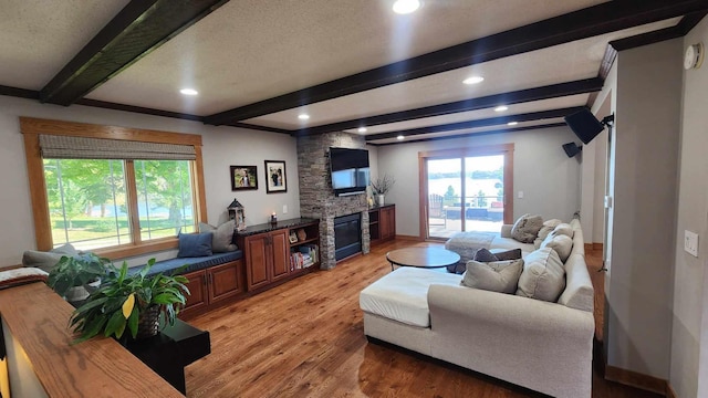 living room featuring beamed ceiling, a fireplace, light wood-type flooring, and a healthy amount of sunlight