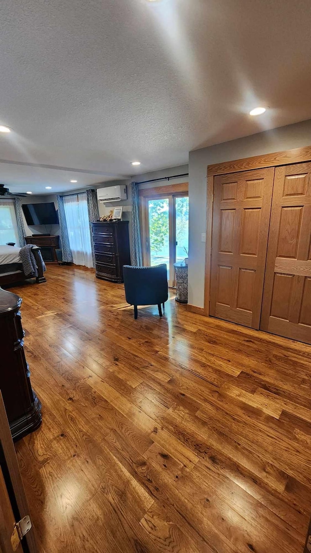 unfurnished living room with wood-type flooring, a textured ceiling, and a wall mounted AC