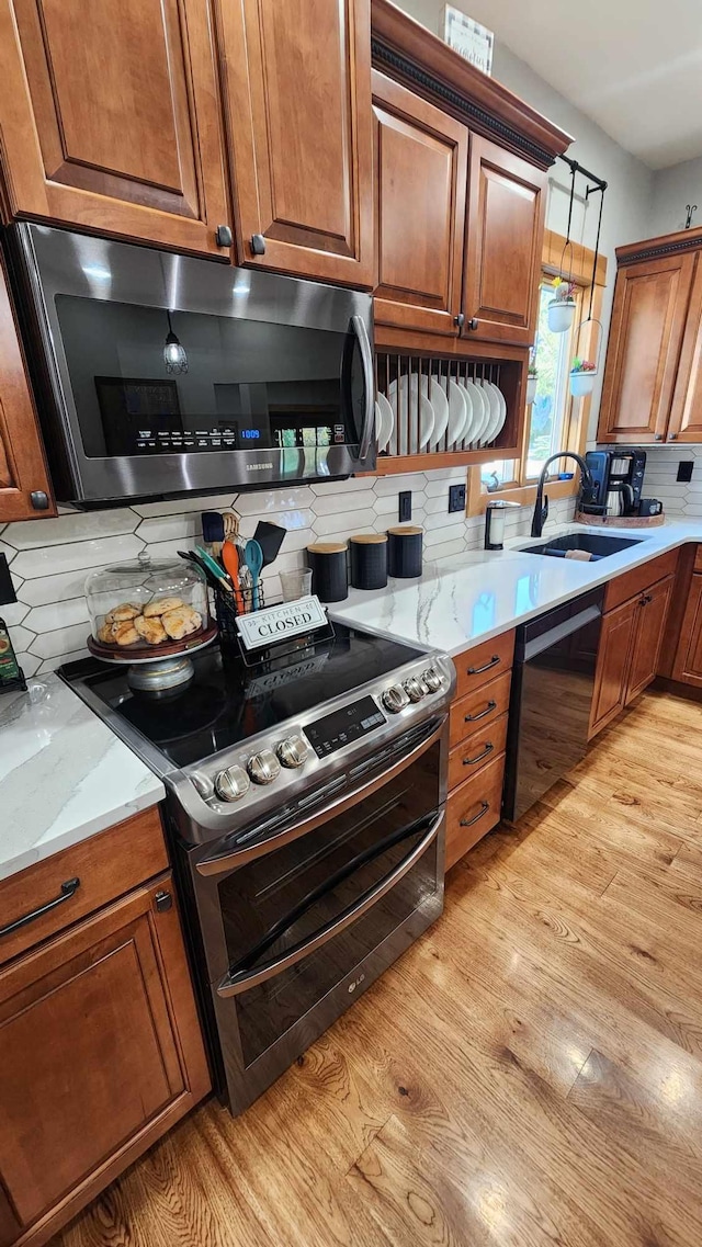 kitchen featuring light stone counters, sink, light hardwood / wood-style flooring, stainless steel appliances, and decorative backsplash