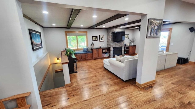 living room with light hardwood / wood-style floors, a fireplace, beamed ceiling, and a wealth of natural light