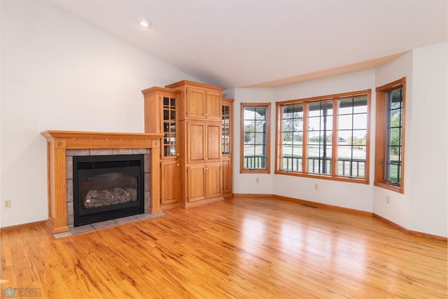 unfurnished living room featuring light wood-type flooring, vaulted ceiling, and a tiled fireplace