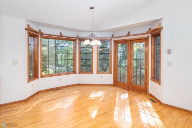 unfurnished dining area with a healthy amount of sunlight, lofted ceiling, hardwood / wood-style floors, and a chandelier