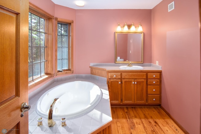 bathroom with hardwood / wood-style flooring, tiled bath, and vanity