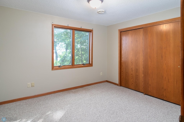 unfurnished bedroom featuring light colored carpet, a textured ceiling, and a closet