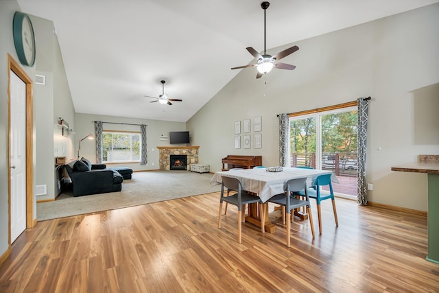 dining room with a stone fireplace, ceiling fan, high vaulted ceiling, and light hardwood / wood-style floors