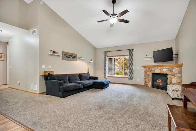 carpeted living room with high vaulted ceiling, a stone fireplace, and ceiling fan