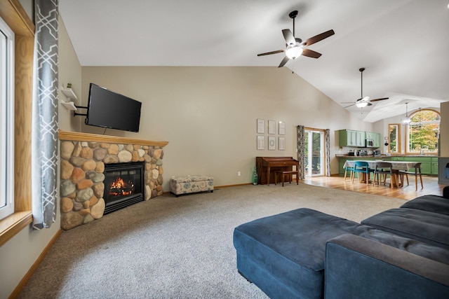 carpeted living room featuring a stone fireplace, ceiling fan, and high vaulted ceiling