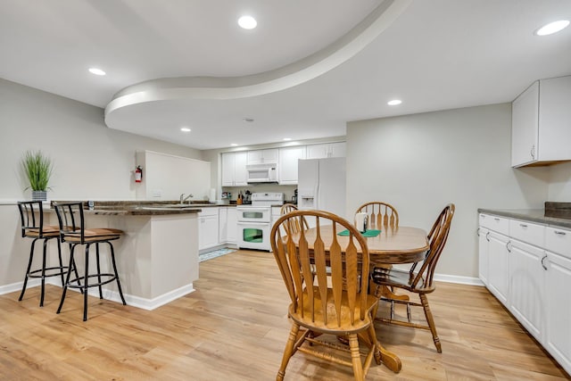 kitchen with a breakfast bar, light hardwood / wood-style flooring, white cabinets, and white appliances