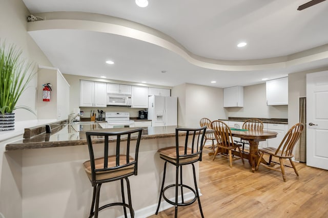 kitchen featuring white appliances, dark stone counters, white cabinets, light wood-type flooring, and kitchen peninsula