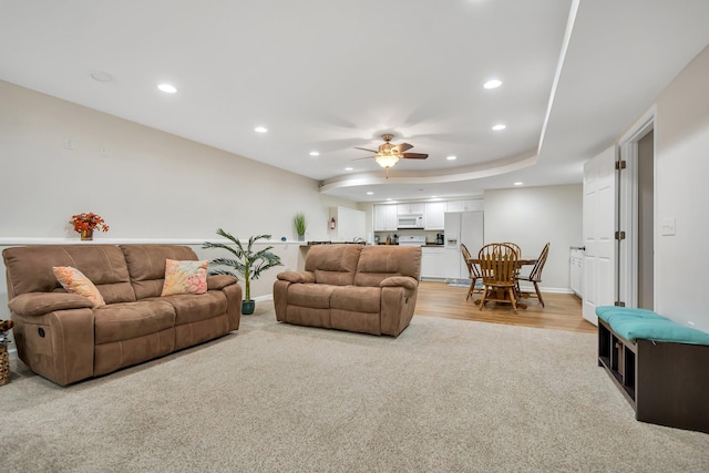 living room with a tray ceiling, ceiling fan, and light wood-type flooring