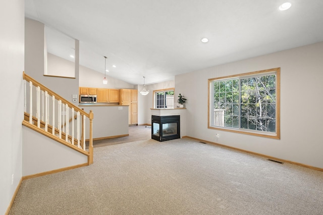 unfurnished living room with a multi sided fireplace, vaulted ceiling, and light colored carpet