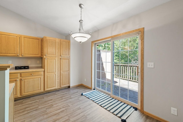 kitchen with light wood-type flooring, lofted ceiling, light brown cabinets, and decorative light fixtures