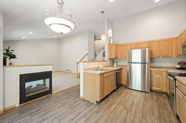 kitchen with sink, a tiled fireplace, kitchen peninsula, hanging light fixtures, and appliances with stainless steel finishes