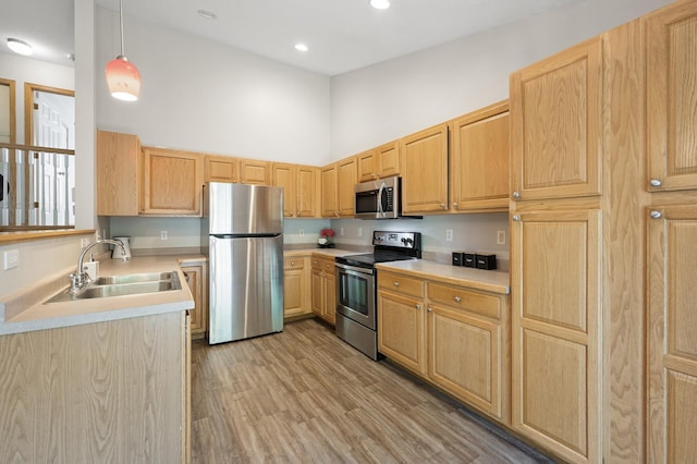 kitchen with appliances with stainless steel finishes, light hardwood / wood-style floors, a towering ceiling, light brown cabinets, and decorative light fixtures