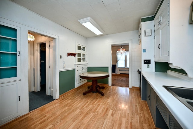 kitchen with light wood-type flooring, a notable chandelier, sink, hanging light fixtures, and white cabinets