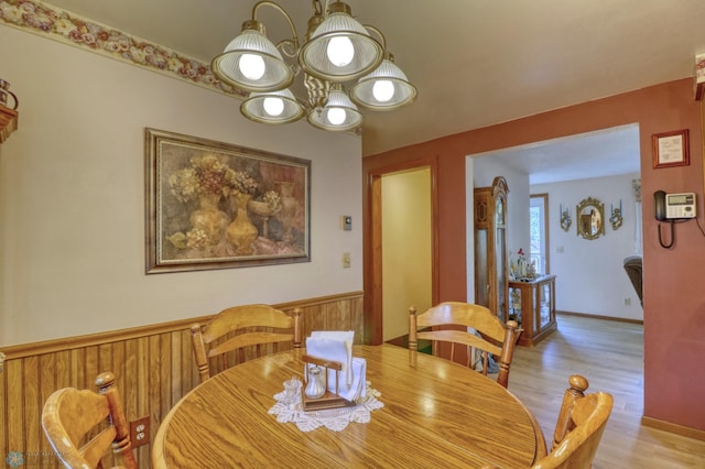 dining space with light wood-type flooring, a chandelier, and wooden walls