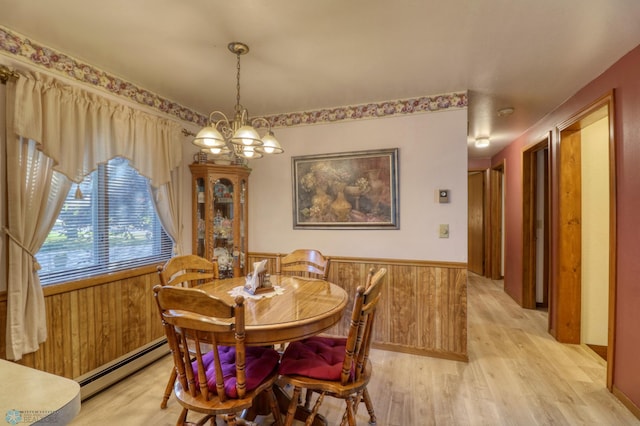 dining area with a baseboard radiator, light wood-type flooring, wood walls, and a chandelier