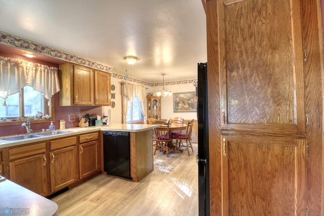 kitchen with sink, kitchen peninsula, decorative light fixtures, black appliances, and light wood-type flooring