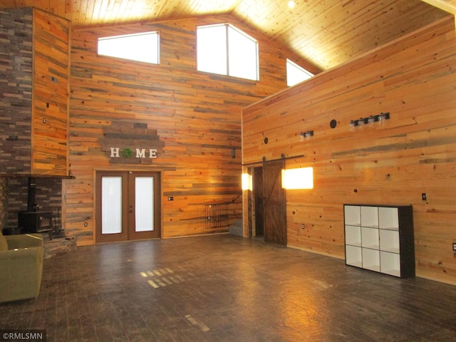 unfurnished living room with wood walls, french doors, a barn door, and a wood stove