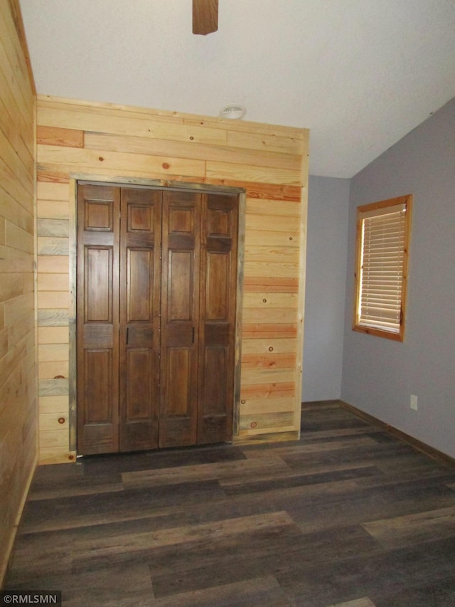 unfurnished bedroom with lofted ceiling, wooden walls, and dark hardwood / wood-style flooring