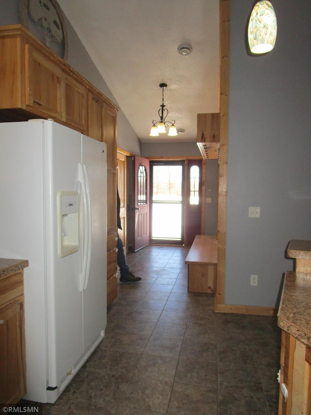 kitchen featuring vaulted ceiling, pendant lighting, a chandelier, dark tile patterned floors, and white fridge with ice dispenser