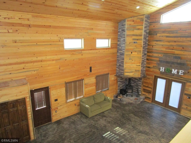 unfurnished living room with wooden ceiling, wood walls, visible vents, vaulted ceiling, and a wood stove