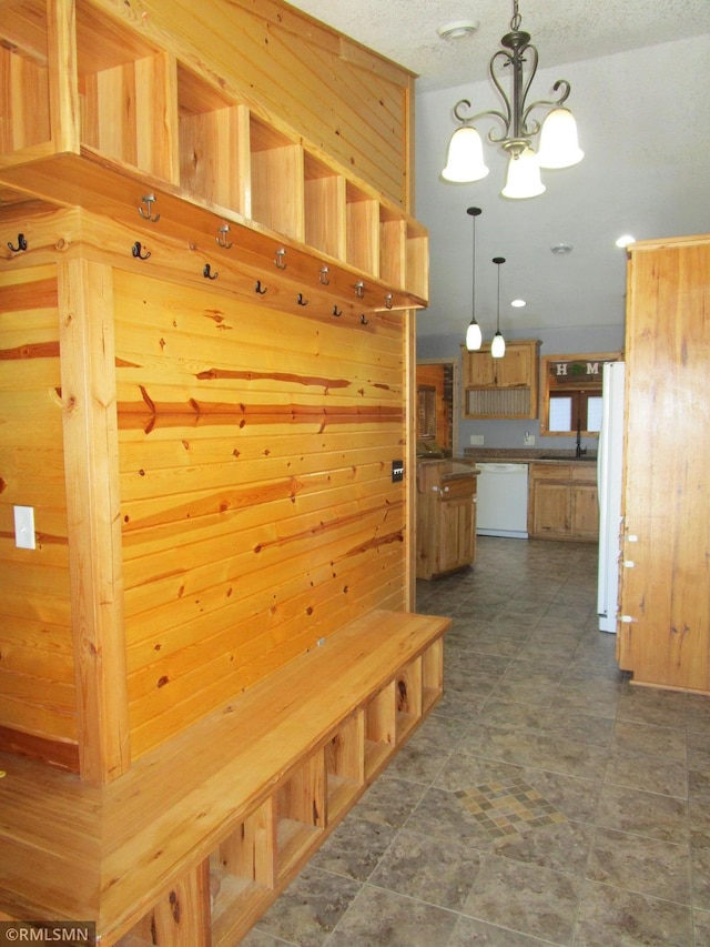 mudroom with an inviting chandelier, wooden walls, and a sink