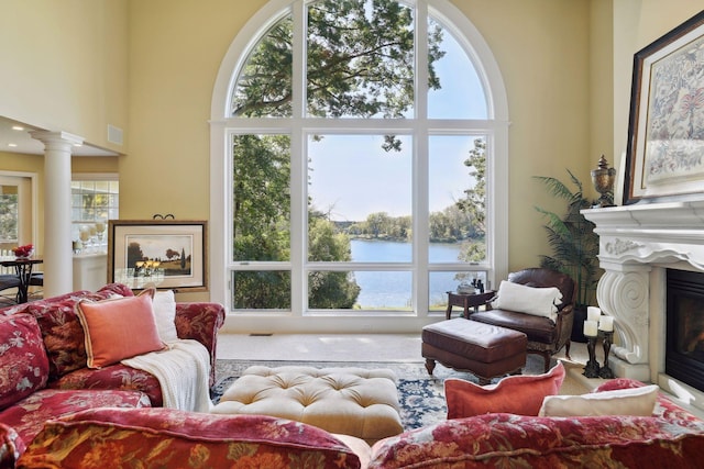 living room with a water view, a towering ceiling, and decorative columns