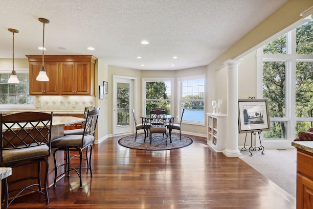 dining room with decorative columns, dark wood-type flooring, a water view, and a textured ceiling