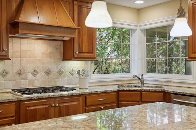 kitchen featuring hanging light fixtures, light stone counters, appliances with stainless steel finishes, premium range hood, and sink