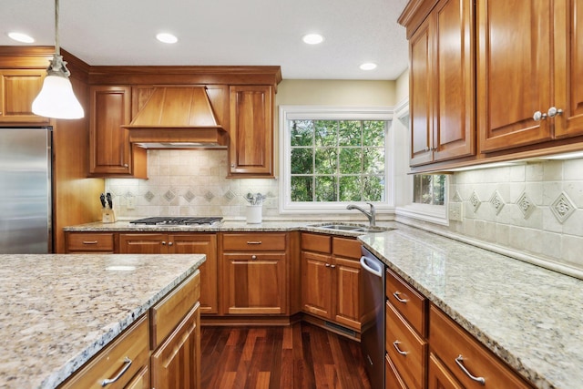 kitchen featuring appliances with stainless steel finishes, premium range hood, sink, dark wood-type flooring, and decorative light fixtures