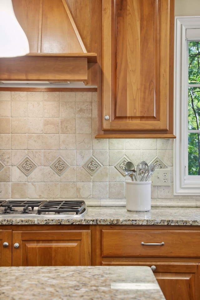 kitchen with light stone counters, custom range hood, stainless steel gas stovetop, and tasteful backsplash