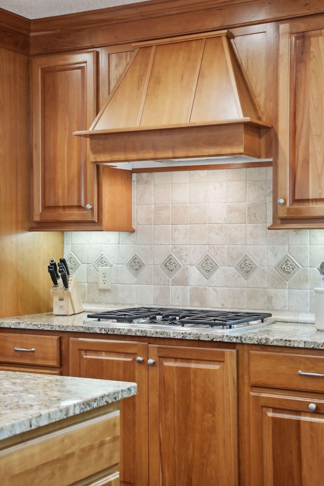 kitchen with light stone counters, premium range hood, stainless steel gas cooktop, and backsplash