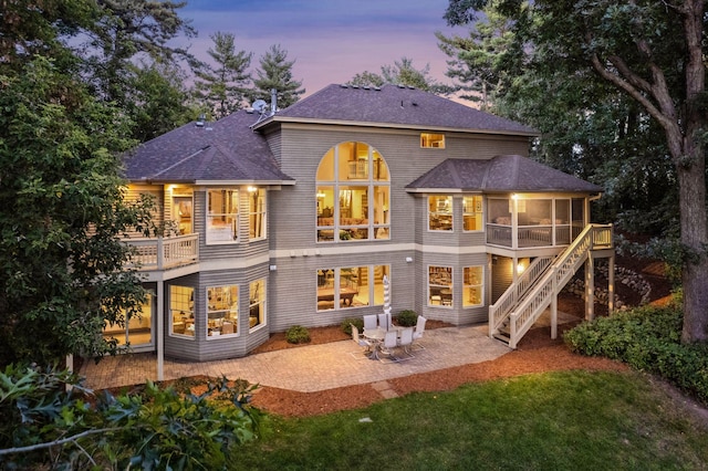 back house at dusk featuring a patio area, a yard, and a sunroom